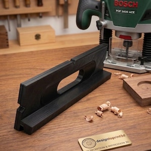 May include: A black woodworking jig with a handle, a Bosch POF 1400 ACE router, and a wooden block with a circular cutout are on a wooden workbench. Wood shavings and a metal hinge are also present. A brass plate reads "designtoprint3d".