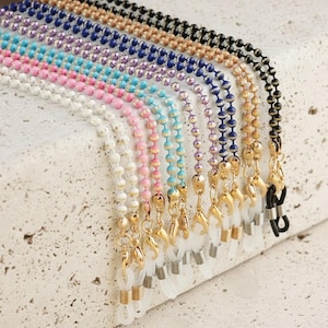 Peut inclure: Une collection de chaînes à lunettes perlées multicolores avec de petites perles rondes et texturées en blanc, rose, turquoise, violet, bleu, or et noir. Chaque chaîne est dotée de fermoirs mousquetons dorés et de boucles en silicone transparent.