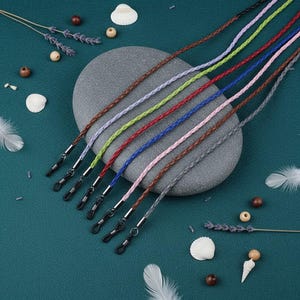 Peut inclure: Un ensemble de huit cordons tressés aux couleurs marron, lavande, vert lime, rouge, bleu, rose, marron foncé et gris. Chaque cordon est doté d'un connecteur en métal noir à une extrémité, conçu pour maintenir des lunettes avec une boucle.