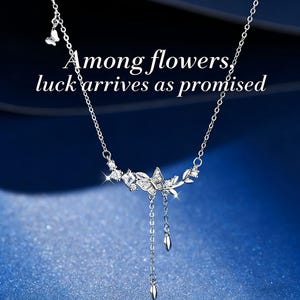 May include: A silver necklace with a butterfly and leaf design, adorned with sparkling crystals. The necklace has a delicate chain and dangling teardrop-shaped charms. The text "Among flowers, luck arrives as promised" is displayed on the image.