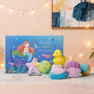 Può includere: Una scatola di MELAO BATH BOMBS con un'illustrazione di sirena, accompagnata da una papera di gomma gialla e varie bombe da bagno a forma di stella, sfera, cuore e conchiglia. Le bombe da bagno sono nelle tonalità del blu, rosa e giallo.