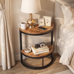 May include: A two-tiered, half-circle side table with a distressed wood finish and black metal frame. The top shelf holds a lamp, mug, and framed photos. The lower shelf displays books and a camera. A bedroom setting.