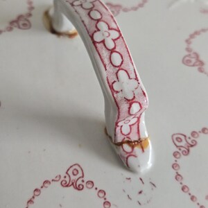Puede incluir: Primer plano de una tapa de cer&aacute;mica blanca con un asa decorativa. El asa es blanca con un estampado floral rojo. La tapa tiene un dise&ntilde;o floral rojo alrededor de los bordes y es de estilo vintage.