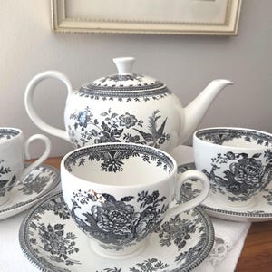 Peut inclure: Un service à thé en porcelaine blanche orné d'un motif floral et d'oiseaux en transfert noir. L'ensemble comprend une théière avec couvercle et trois tasses assorties avec soucoupes. Chaque pièce présente des illustrations botaniques détaillées.