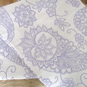 Puede incluir: Tela blanca con un patrón paisley morado. La tela está doblada por la mitad y el patrón es visible en ambos lados.