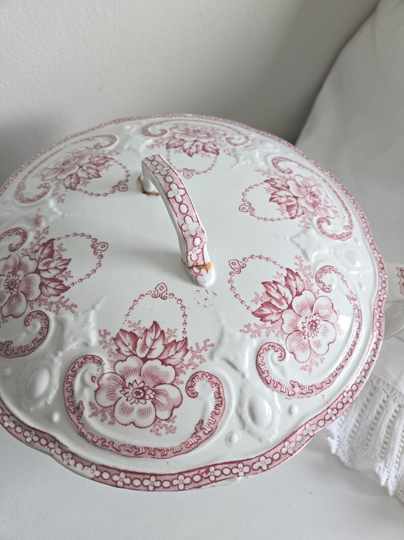 Puede incluir: Tapa de fuente de cer&aacute;mica blanca con un estampado floral rosa. La tapa tiene un asa decorativa y un borde festoneado. El dise&ntilde;o floral incluye flores grandes y peque&ntilde;os detalles florales.