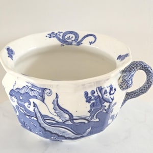 May include: White and blue porcelain chamber pot with a dragon design. The pot has a wide rim and a handle with a scale pattern. The blue design depicts dragons and waves.