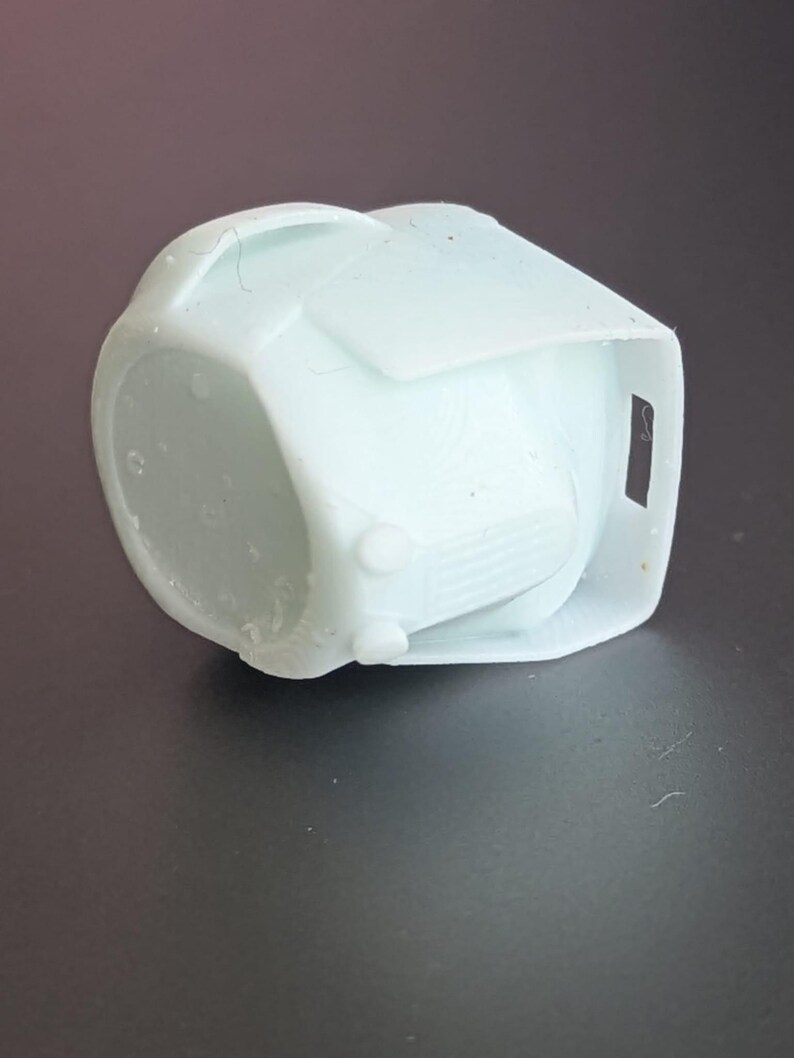 May include: A light blue, geometric-shaped object with a rounded base and a rectangular top. The object has a small, rectangular opening on one side and two small, circular protrusions on the front. The object appears to be made of plastic.
