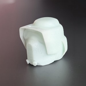 May include: A light green, 3D-printed helmet with a rounded top and a visor-like brim. The helmet has a textured surface and a detailed front, suggesting a futuristic or sci-fi theme. The object is set against a dark background.