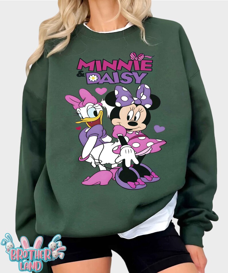 May include: Dark green sweatshirt featuring Minnie Mouse and Daisy Duck. The graphic includes the text "MINNIE & DAISY" in pink and purple, with a daisy and hearts. The characters are in their signature outfits.