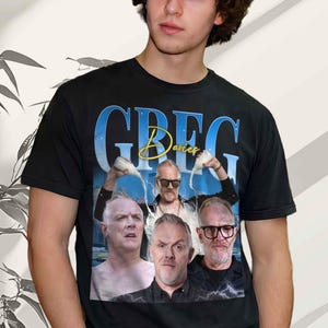 May include: Black t-shirt with a design featuring Greg Davies. The name "GREG Davies" is displayed in blue and gold lettering. The design includes multiple images of the comedian, with a blue and white background.