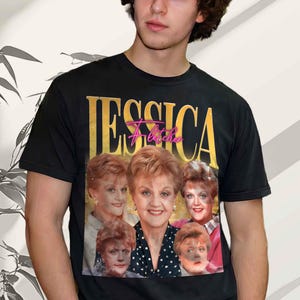 Puede incluir: Una camiseta negra de manga corta con un estampado gráfico de Jessica Fletcher. El diseño incluye el nombre JESSICA en letras doradas grandes, el nombre Fletcher en letra cursiva rosa y un collage de cinco retratos diferentes del personaje.