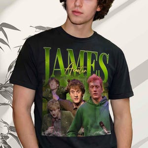Puede incluir: Camiseta negra con un diseño de James Acaster. El diseño presenta el nombre "JAMES" en letras verdes grandes y "Acaster" en una fuente cursiva más pequeña. La camiseta tiene cuello redondo y mangas cortas. El diseño incluye imágenes de James Acaster.