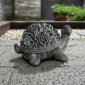 May include: A gray stone turtle planter with a detailed shell design filled with sculpted flowers. The turtle has a textured surface and is positioned on a stone patio. The planter is designed for outdoor use and adds a decorative touch to gardens.