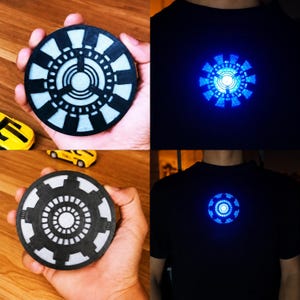 Pode incluir: Um acessório de reator de arco circular com um design geométrico em preto e branco. O dispositivo é mostrado desligado e também como uma luz azul brilhante fixada no centro de uma camiseta preta lisa, criando um efeito circular luminoso.
