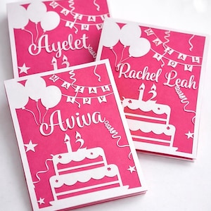 May include: Three pink birthday cards with white cut-out designs. Each card features a name, the number 13, a cake, balloons, and a banner. The names are Ayelet, Aviva, and Rachel Leah. Stars and ribbons complete the festive look.