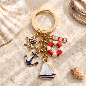 May include: A gold-toned metal keychain featuring five nautical-themed charms: a ship wheel, a dark blue anchor, a red and white striped lighthouse, a red and white lifebuoy, and a white sailboat with blue trim, all attached to a circular ring.