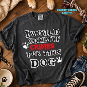 May include: Charcoal grey t-shirt with the slogan "I WOULD COMMIT CRIMES FOR THIS DOG" in white and red. The image includes a dog bowl, leash, and jeans, suggesting a pet-themed product.