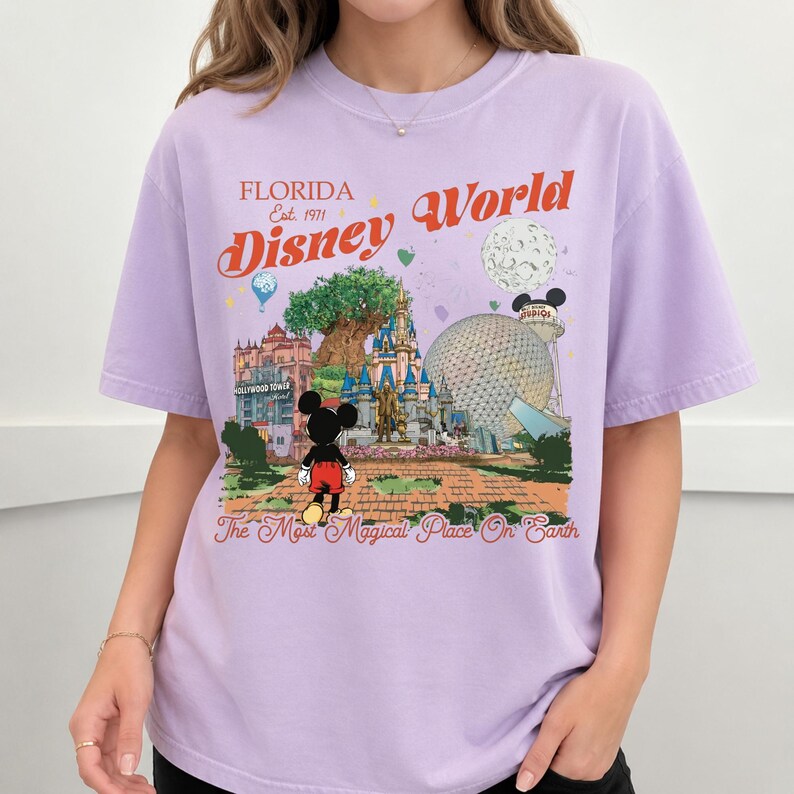 May include: A light purple t-shirt featuring a colorful graphic of Disney World in Florida. The design includes the text "Florida Disney World" and "The Most Magical Place On Earth", along with images of Mickey Mouse and park landmarks.