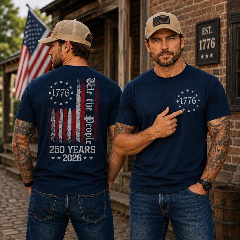 Op de afbeelding: Een marineblauw t-shirt met een verweerde Amerikaanse vlag op de achterkant met de tekst We the People, 1776 en 250 YEARS 2026. De voorkant van het shirt toont een kleine cirkelvormige afbeelding met 1776 omringd door dertien sterren.