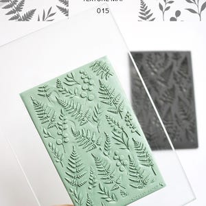 May include: A sage green rectangular texture mat featuring an embossed pattern of various ferns and botanical sprigs. The mat is held behind a clear acrylic sheet. Text on the packaging reads DASHA PARADOKS TEXTURE MAT 015.