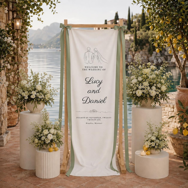 K&ouml;nnte beinhalten: Ein Hochzeitsschild mit dem Text "Welcome to the Wedding of Lucy and Daniel" in schwarzer Schrift. Das Schild befindet sich auf einem Holzrahmen mit gr&uuml;nen B&auml;ndern und ist von wei&szlig;en Blumengestecken und Zitronenb&auml;umen umgeben.