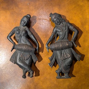 May include: Two black metal sculptures of dancers holding drums. The sculptures are detailed and have intricate designs.