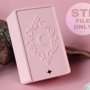 Puede incluir: Una caja rectangular de color rosa claro con un marco decorativo en relieve que presenta una luna creciente en el centro y una estrella de cuatro puntas en la parte inferior. La caja tiene un acabado liso e incluye un gráfico circular con el texto STL FILE ONLY.