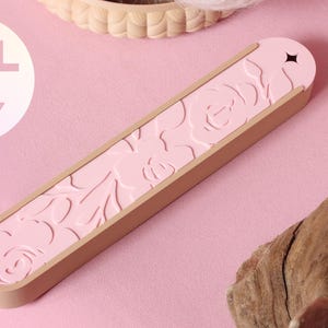 May include: A light pink, elongated, rectangular case with rounded ends, featuring a debossed floral pattern on the top surface and a small star-shaped cutout at one end. A circular white graphic displays the text STL FILE ONLY.