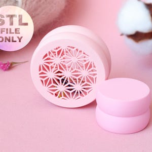 Puede incluir: Un objeto rosa claro impreso en 3D con un diseño geométrico, junto a dos cilindros rosas apilados. El texto "STL FILE ONLY" es visible en una pegatina circular. Los objetos están sobre una superficie rosa.