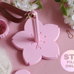 Op de afbeelding: Een roze, bloemvormige pennenhouder met een bruin lederen handvat. Een kleine roze container bevat goudkleurige paperclips. De afbeelding bevat ook witte bloemen en de tekst "STL FILE ONLY".