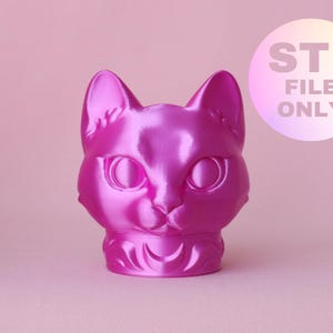 Puede incluir: Una figura de cabeza de gato impresa en 3D de color rosa intenso metálico con ojos grandes y orejas puntiagudas. La base presenta un diseño de luna creciente. Un gráfico circular blanco en la esquina superior derecha contiene el texto STL FILE ONLY.