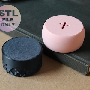 May include: Two small, round containers. One is black with a textured top and a floral pattern on the side. The other is light pink with a cross-shaped cutout on top. The image includes the text "STL FILE ONLY".