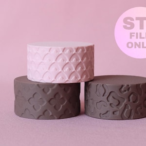 Puede incluir: Tres objetos cilíndricos con patrones en relieve. Un cilindro rosa claro presenta un diseño de escamas, mientras que dos cilindros gris oscuro muestran texturas florales y de leopardo. Un gráfico circular indica STL FILE ONLY.