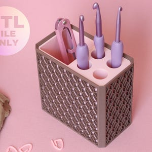 May include: A rectangular brown organizer with a geometric lattice pattern on the exterior and a light pink interior. It features a top insert with circular holes holding three lavender crochet hooks and a pink tool. Text reads STL FILE ONLY.