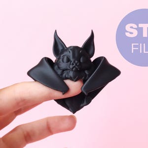 May include: A matte black 3D printed bat figurine with pointed ears and folded wings. The bat is designed to rest on a finger. A circular purple badge in the upper right corner contains the white text STL FILE, indicating a digital download.