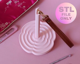 May include: A light pink yarn holder with a brown leather strap and gold-colored clasp. The holder has a flower-like design. The image also includes a pink case, scissors, and a crochet hook. The text "STL FILE ONLY" is visible.