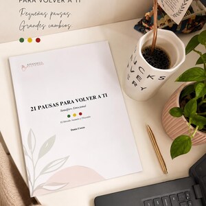 Puede incluir: Un libro blanco titulado 21 PAUSAS PARA VOLVER A TI con un gráfico de puntos verde, amarillo y rojo. La portada presenta una ilustración de hojas y el nombre de la autora Dania Cossio. Cerca hay una taza, un bolígrafo dorado y una planta.