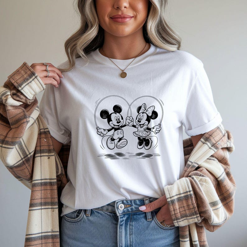 Puede incluir: Camiseta blanca con una ilustraci&oacute;n en blanco y negro de Mickey y Minnie Mouse saltando a la cuerda. El dise&ntilde;o muestra a los personajes sosteniendo cuerdas de saltar, formando un coraz&oacute;n. Tema de dibujos animados cl&aacute;sico.