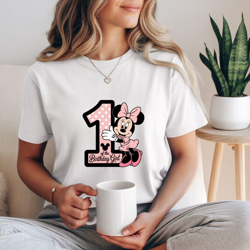 May include: White t-shirt featuring a graphic of Minnie Mouse with a pink polka-dotted number 1 and the text "of the Birthday Girl". Minnie Mouse is wearing a pink dress and bow. The shirt is a birthday-themed item.