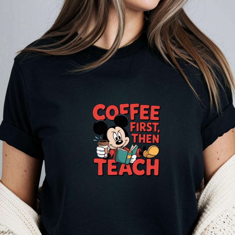 May include: Black t-shirt with a cartoon Mickey Mouse design. Mickey is holding a coffee cup and a book. The red text reads "COFFEE FIRST, THEN TEACH". The design is centered on the shirt.