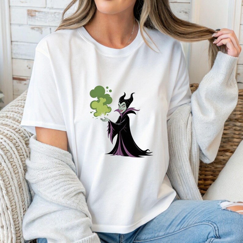 May include: White t-shirt featuring a cartoon illustration of a character in a black and purple gown with a green cloud of smoke. The character has a stern expression and is holding the smoke in their hand.