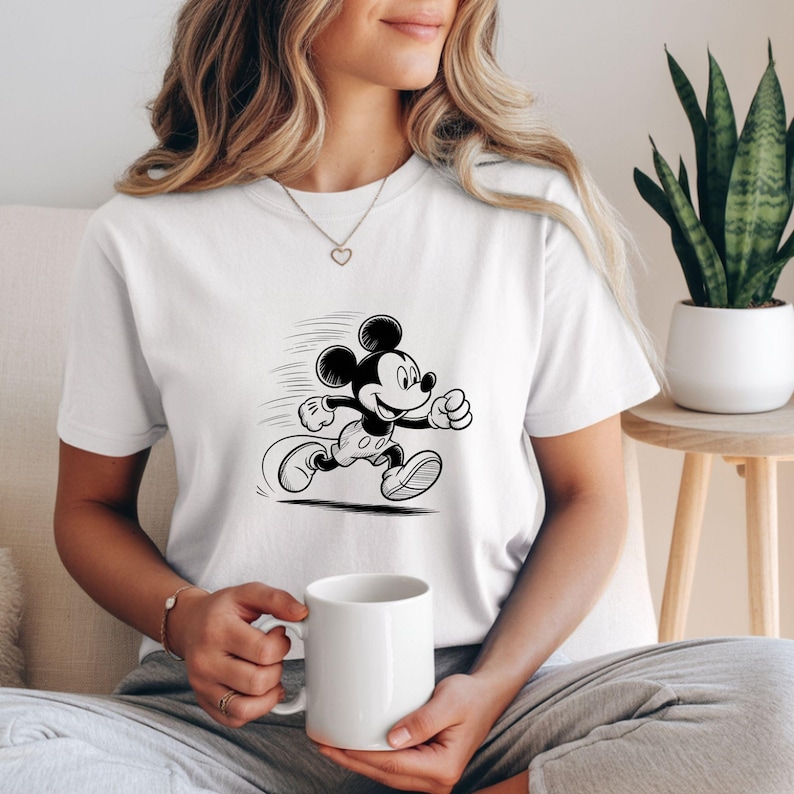 K&ouml;nnte beinhalten: Wei&szlig;es T-Shirt mit einer Schwarz-Wei&szlig;-Illustration von Mickey Mouse beim Laufen. Die Zeichentrickfigur wird in Bewegung mit Geschwindigkeitslinien dargestellt. Das T-Shirt hat einen klassischen Rundhalsausschnitt.