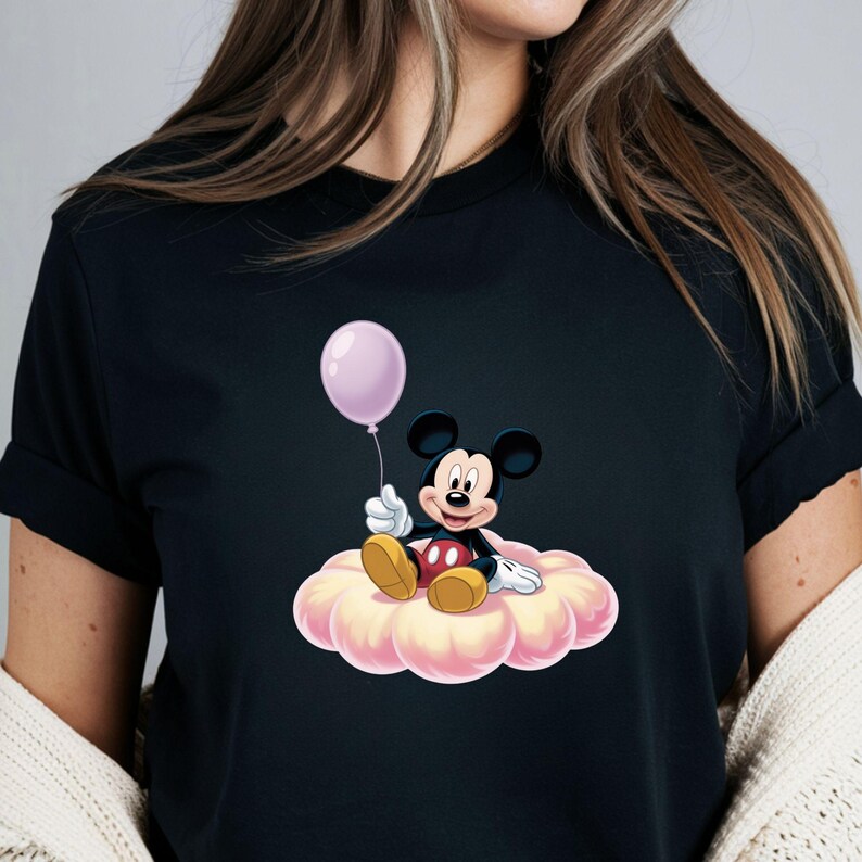 May include: Black t-shirt featuring a cartoon illustration of Mickey Mouse sitting on a pink cloud and holding a light purple balloon. Mickey Mouse is wearing red shorts, yellow shoes, and white gloves.