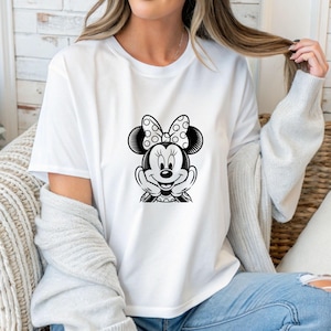 May include: White t-shirt featuring a black and white Minnie Mouse graphic. The graphic shows Minnie Mouse with her hands under her chin, wearing a polka dot bow. The shirt is a classic crew neck style.