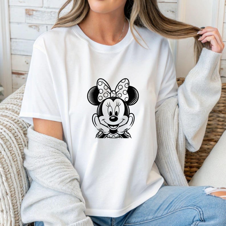 May include: White t-shirt featuring a black and white Minnie Mouse graphic. The graphic shows Minnie Mouse with her hands under her chin, wearing a polka dot bow. The shirt is a classic crew neck style.