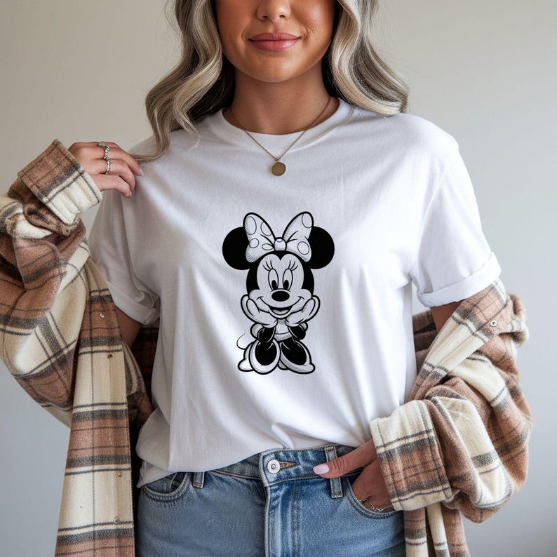 May include: White t-shirt featuring a black and white Minnie Mouse graphic. The cartoon character is smiling and wearing a bow. The shirt is a classic crew neck style.