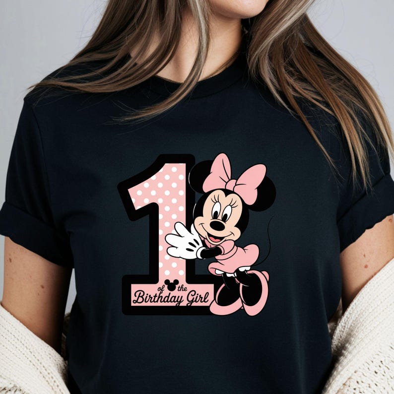 May include: Black t-shirt featuring a graphic of Minnie Mouse in a pink dress and bow, with a large number 1 in pink polka dots. The text "of the Birthday Girl" is below the number.