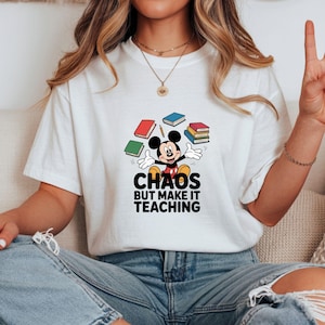 May include: White t-shirt with a Mickey Mouse graphic, books, and the text "Chaos But Make It Teaching". The design includes red, green, and blue books. This casual t-shirt is suitable for everyday wear.