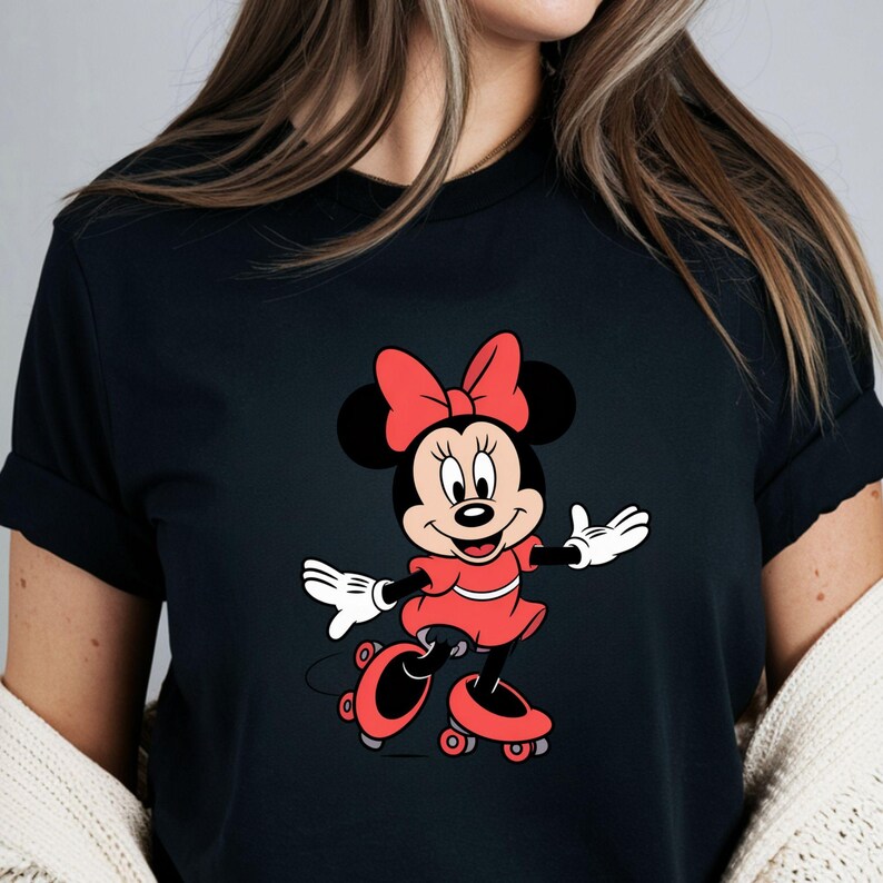 May include: Black t-shirt featuring a cartoon illustration of Minnie Mouse in a red dress, bow, and roller skates. Minnie Mouse is smiling with her arms outstretched. The design is centered on the shirt.